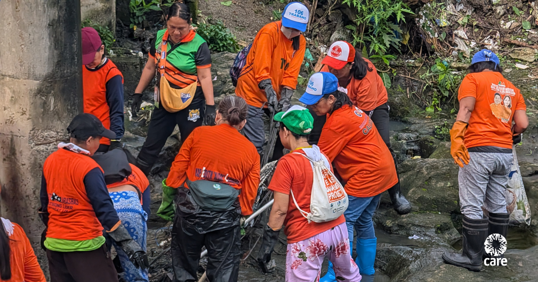 A group of volunteers wearing gloves and holding brooms cleaning a riverside area in Caloocan City